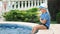 Slow motion little boy in sunglasses and hat sitting on edge of swimming pool playing legs in water