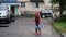 SLOW MOTION:  little girl in pink rubber boots have fun jumping in a puddle. nearby are the cars in the yard of a large new brick