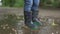 SLOW MOTION, LOW ANGLE, CLOSE UP, DOF: Carefree little boy in grey rain boots jumps into the big puddle. Unrecognizable