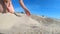 Slow motion. Low angle. Girl picks up handful of sand in her palm