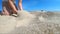 Slow motion. Low angle. Girl picks up handful of sand in her palm