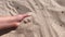 Slow motion. Low angle. Girl picks up handful of sand in her palm a