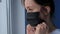 Slow motion: pensive woman putting on black face mask and looking out of window