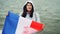 Slow motion portrait of cheerful French patriot holding official flag of France with cute smile standing near the water