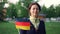 Slow motion portrait of cheerful young woman waving official German flag and looking at camera while standing in nice