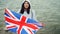 Slow motion portrait of glad tourist visiting Great Britain holding British national flag and smiling standing on sea