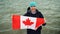 Slow motion portrait of joyful young man traveller holding Canadian flag in hands and looking at camera with glad smile