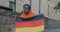 Slow motion portrait of patriotic African American man waving German national flag smiling outdoors in city