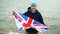 Slow motion portrait of patriotic Englishman holding flag of Great Britain standing on sea coast and smiling happily