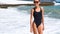 Slow motion portrait slender beautiful smiling woman in swimwear standing in water on sea beach