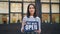 Slow motion portrait of smiling young woman entrepreneur holding we are open sign standing outdoors in front of her new