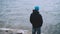 Slow motion portrait of young man tourist standing on the sea shore and looking at waves on cold windy day. People