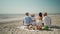 slow motion rear view four happy friends, wto couples sitting on picnic blanket with food on foreground and kissing