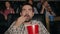 Slow motion of scared guy eating popcorn watching shocking movie in cinema