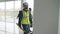 Slow motion of serious builder walking inside empty office center wearing uniform and carrying tool