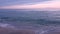 Slow motion shooting of the sunset at sea. Blue clouds over water pink blue horizon. Small waves reach the shore. Travel holidays