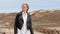 Slow motion shot of concerned woman walking in dunes and looking around. Wind shakes blond hair.