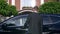 Slow motion of slender handsome businessman walking and sitting to the black car standing near beautiful house