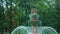 Slow motion of streams of water falling in fountain. Green trees of park at background.