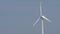 Slow motion wind turbine blades rotate against a blue sky