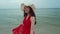 Slow-motion of woman with arms spread in a red dress on sea beach with wind blow