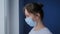 Slow motion: woman with face mask suffering from coughing, looking out of window