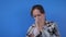 Slow motion: woman feeling sick, sneezing into facial tissue against blue wall