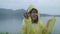 Slow motion - Young Asian woman feeling happy playing rain while wearing raincoat standing near lake.