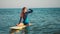 Slow motion: young slim surf girl looking at sunset. Floats on a yellow board in the open sea, waits for a wave and