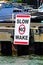 A slow no wake sign on a dock with boats in the background