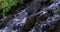 Slow vertical pan of fast water flowing downhill between rough rocks on a rocky terrain in Utah Valley forest