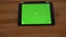 Slowly approaching close-up shot of horizontal tablet with green screen on wooden desk background.