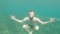 Slowly moving a young bearded man tries to meditate in a lotus pose at the bottom of the sea in the water. The concept