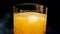 Slowly rotating glass with yellow-orange sweet multifruit juice and ice cubes