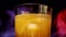Slowly rotating glass with yellow-orange sweet multifruit juice and ice cubes