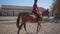 Slowmo of a Caucasian girl in pink clothes and helmet riding brown horse in the corral. Young female equestrian resting