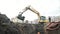 Slowmotion excavator digging ditch with two workers in orange hats in it