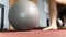 A slowmotion shot of a big pilates ball getting kicked by a foot at a gym