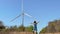 Slowmotion shot of a woman standing on a road leading to the wind electric generator. Investment in green energy. Green