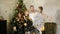 Slowmotion shot of young happy family of four by the Christmas tree throwing up golden confetti. Cute mother, father and