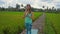 Slowmotion steadicam shot of a young woman with yoga math walking through a beautiful rice field