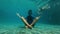 Slowmotion underwater shot of a young man in a yoga pose meditating on the bottom of a swimming pool. He is disturbed by