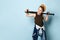 Sly little schoolboy stands near the wall looking aside holding baseball bat on shoulders. portrait isolated on blue background