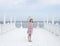 Small 8 years old pretty cheerful girl in a dress with a floral print and in yellow sunglasses stands on a wooden white pier