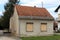 Small abandoned family house with dilapidated facade and two front windows covered with window blinds surrounded with grass and