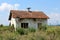 Small abandoned red bricks house with dilapidated white facade and destroyed roof tiles completely surrounded with high grass