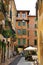 a small alley in an Italian city, a courtyard between tenement houses, green shutters, greenery on the balconies,