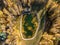 Small artificial reservoir pond for fishing with boat surrounded by golden autumn foret trees and cottage houses. Aerial drone