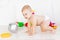 A small baby boy six months old crawls through in a light white nursery in diapers among toys