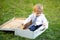 Small baby boy in suit and necktie tie sitting in huge suitcase. Child baby playing on sunny field, summer outdoor kids